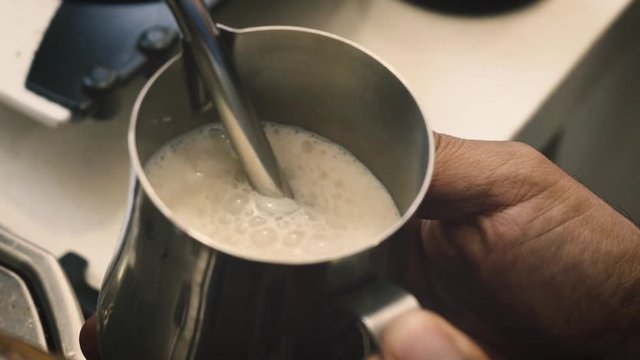 Barista holding a jug of foam texturing milk with the machine vaporizer. view from the left side
