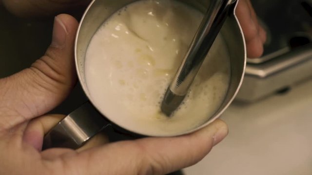 Barista holding a jug of foam texturing milk with the machine vaporizer, view from the top