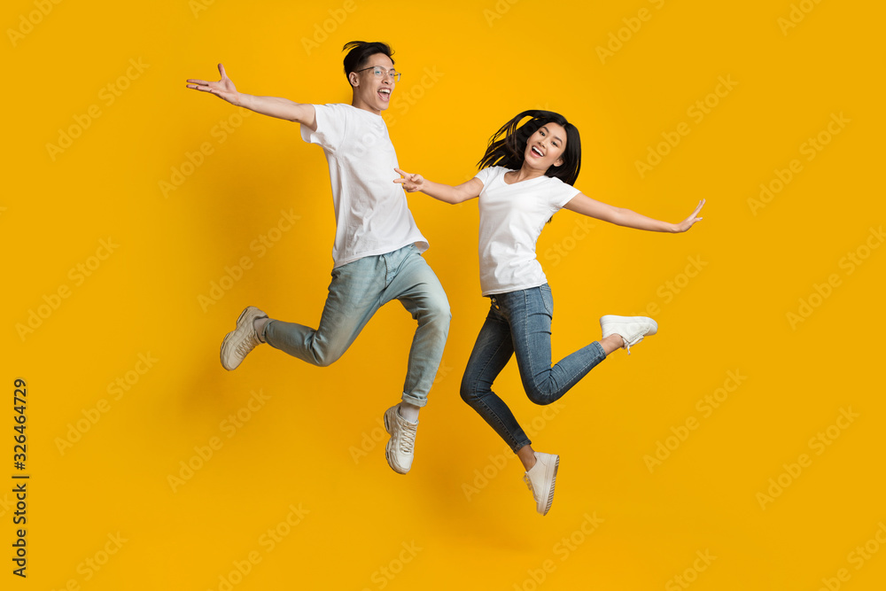 Wall mural emotional asian couple jumping over yellow background