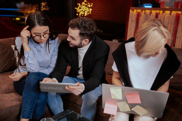 On the modern work office studio one good looking guy and pretty lady smiling have a break time sitting on the stairs have, looking at the pictures on tablet