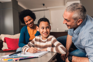 Parents helping their son with his homework at home in living room.