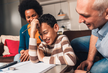 Parents helping their son with his homework at home in living room.