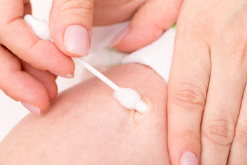 Mother wipes newborn baby navel with cotton swab