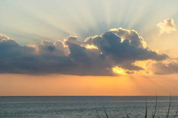 Sunset over the sea in Bali, Indonesia. There is a cloud, behind which the sun is hiding. The sunbeams are spreading in each direction. There is a bird flying above the sea surface. Golden hour