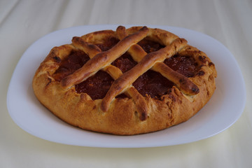 Baking: sweet cake with fruit filling from apple jam. The cake is shown on a light cream background and lies on a white plate.