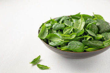 Fresh spinach leaves in a bowl on a white background