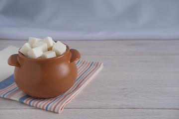 A small brown pot filled with lump sugar on a light countertop and a striped towel.