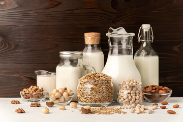 Different types of lactose-free vegetarian dairy products. Milk from macadamia, chickpeas, oats, walnuts and almonds on a brown wooden background. Proper nutrition concept. Copy space.