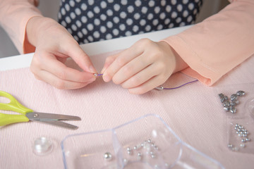 kid weaves a bead bracelet on a white table with a pink cloth and a container for beads in candy style