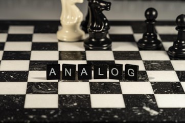 Analog the word or concept represented by black and white letter tiles on a marble chessboard with chess pieces