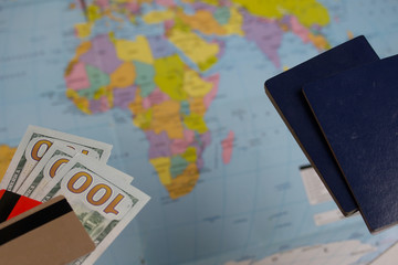 Two passports, one hundred dollar bills and bank cards. Against the background of a world map. Silhouettes of continents are visible.