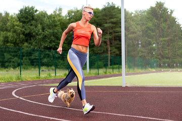 Obraz premium An adult woman runs in the stadium, with a little dog.