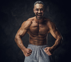 Fototapeta na wymiar Strong, adult, fit muscular caucasian man coach posing for a photoshoot without his shirt in a dark studio under the spotlight wearing sporty shorts, showing his muscles looking powerful and roaring