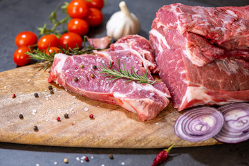 raw meat and vegetables on cutting board on dark cement background