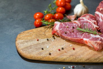 raw meat and vegetables on cutting board on dark cement background