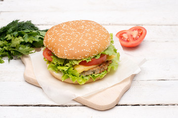 Closeup of a fresh homemade better burger on an old white wooden board with tomato, cheese and red onion.