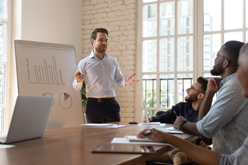 Business trainer stands in front of diverse team makes presentation
