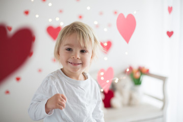 Cute blonde toddler boy, holding box in heart shape and flowers