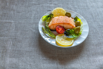 Salmon grilled steak garnished with greens on background of gray rustic linen napkin. Selective focus on piece of fish. No AI tools were used