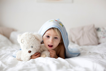 Cute little toddler boy, relaxing in bed after bath, smiling happily, daytime