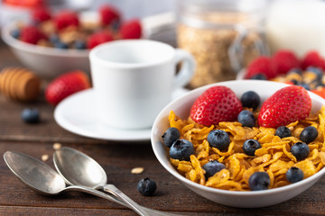 Healthy breakfast of cornflakes cereals with blueberries and strawberries with white cup behind.