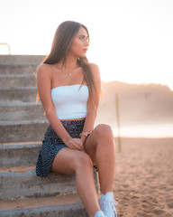 Lifestyle, a smiling young brunette with a white top sitting on the beach looking towards the horizon