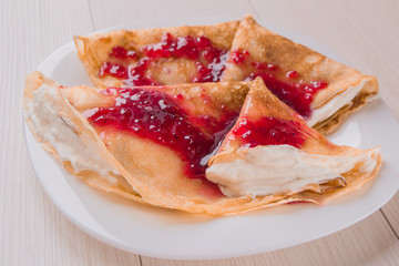 Classic traditional Russian pancakes with whipped cream and raspberry jam ready to serve....