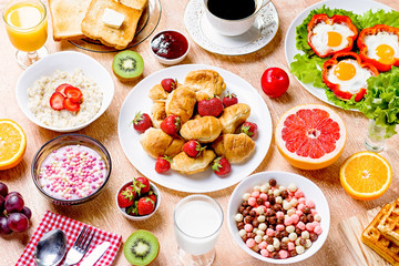 Continental breakfast with cereal, fried eggs, croissants, fruits and drinks on textured table, copy space. Table top with various healthy snacks and foods on rustic background