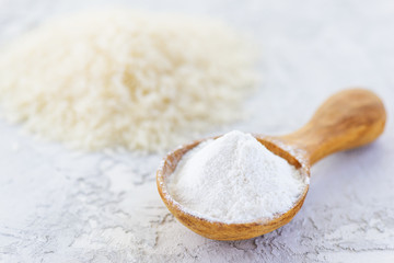 Rice flour in a wooden spoon on a gray table. Gluten free, healthy diet concept.