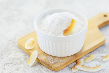 Coconut flour in a bowl with coconut chips on a wooden board. Gluten free, healthy diet concept.
