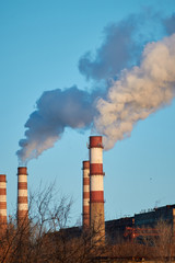 The plant emits smoke and smog from the pipes during a sunny day, pollutants enter the atmosphere. Ecological catastrophy. Harmful emissions. Chemical industry