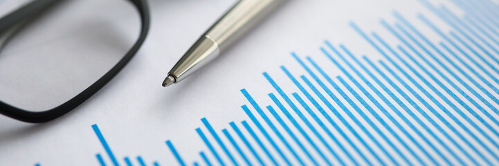 Silver pen with paper chart and glasses lie in office table closeup. Business education concept