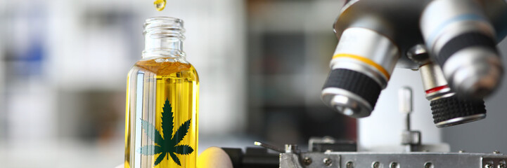 Fototapeta na wymiar Focus on male hand holding glass bottle with cannabinoid oil. Pharmacist dripping medicine drops in flask. Healthcare and marijuana concept. Blurred background