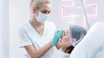 The young beautician doctor preparing to making injection in female forehead. The doctor cosmetologist makes anti-aging treatment and face lift procedure.