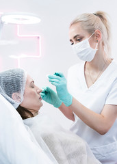 The young beautician doctor preparing to making injection in female forehead. The doctor cosmetologist makes anti-aging treatment and face lift procedure.