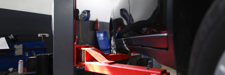 Naklejka premium Close-up of red pillaring stand used for automobiles and sportcars examinations and lifting heavy machinery. Hardworking people mechanics repair differential and engines indoors