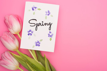 Top view of flowers and card with spring lettering on pink background