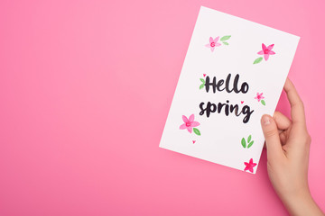 Partial view of card with hello spring lettering in woman hand on pink background