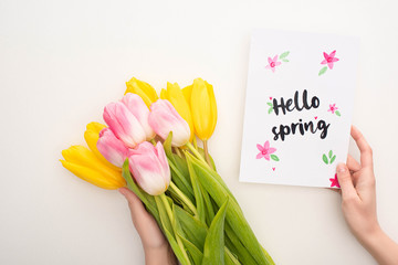 Cropped view of woman holding bouquet of tulips and card with hello spring lettering on white background