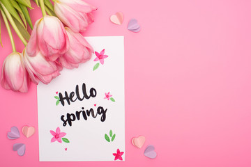 Top view of tulips, card with hello spring lettering and decorative hearts on pink