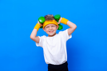 Fitness child. Portrait of sporty little boy with dumbbells over blue studio background. Gym workout. Child sportsman. Childhood activity. Sport. Fitness, health and energy. Success