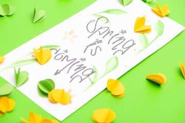 Selective focus of card with spring is coming lettering and decorative hearts on green background