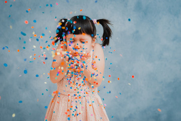 little girl child cheerfully throws up colorful tinsel and confetti on a gray blue background.