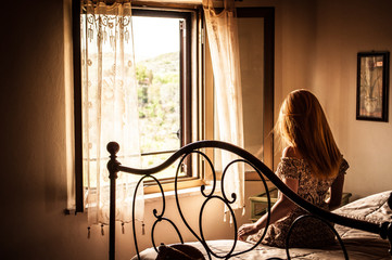 Kobieta siedząca na łóżku i spoglądająca w okno - obrazy, fototapety, plakaty