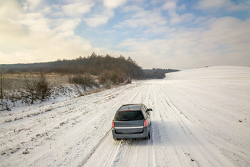 Fototapeta na wymiar Family car driving on a dirt road in snow covered winter field.