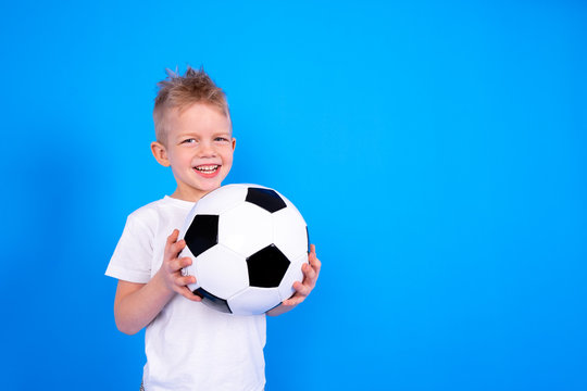 Soccer fans. Smiling caucasian child boy holding soccer ball in hands over blue studio background. Copyspace. Football game