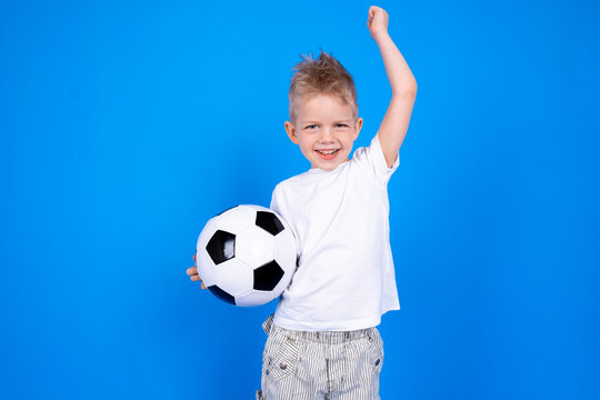 Soccer fans. Cheerful caucasian child boy boy celebrating victory holding soccer ball in hands over blue studio background. Copyspace. Football game