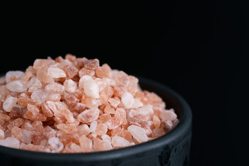 Fototapeta na wymiar Macro shot of pink Himalayan salt in black ceramic bowl. Black background, high resolution