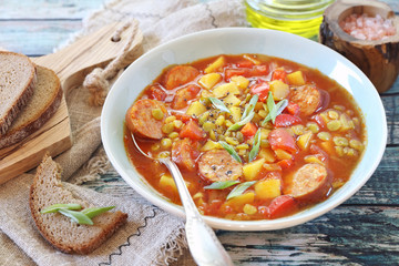 Homemade spicy pea soup with potatoes, tomatoes, sausages and slices of bread