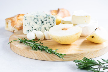 Fresh hot baguette with set of cheeses, rosemary and tomatoes on the serving board close up. Tasty and healthy food concept.